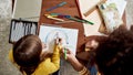 Coloring Dreams. Top view of caucasian little girl spending time with african american baby sitter. They are drawing a