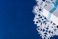 Background of various Christmas themed snowflakes cut out of white paper on a trendy blue background 2020 with a gift Royalty Free Stock Photo