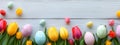 Coloured eggs and coloured tulips on light grey wooden background. Easter style decoration banner. Holiday celebration greeting