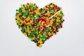 Coloured jelly beans are scattered in the shape of a heart and a lollipop in the form of an arrow on a white background.