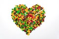 Coloured jelly beans are scattered in the shape of a heart and a lollipop in the form of an arrow on a white background.