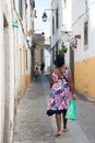Coloured woman seen from her back walking on an old street at Evora, Portugal. Wearing a colorful dress and carrying a plastic bag