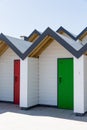 Colourful doors of green and red, with each one being numbered individually, of white beach houses on a sunny day