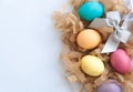 Colourful easter eggs on hay and silver bow over white table. Top view with copy space Royalty Free Stock Photo