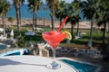 Colourful cold Strawberry daiquiri cocktail drink served in glass at pool bar overlooking blue pool, sea and palm trees, relax and Royalty Free Stock Photo