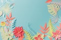 Colourful handmade tropical paper flowers and leaves on blue pastel background with copyspace in the middle, summer spring flower