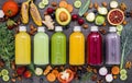 Colourful healthy smoothies and juices in bottles with fresh tropical fruit and superfoods on dark stone background with copy