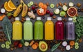 Colourful healthy smoothies and juices in bottles with fresh tropical fruit and superfoods on dark stone background with copy