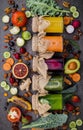 Colourful healthy smoothies and juices in bottles with fresh tropical fruit and superfoods on dark stone background with copy