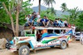 A colourful Jeepney taxi full of people on the roof prepares to leave the rural village