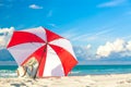 Colourful red and white umbrella with beach bag on the ocean beach against beautiful blue sky and clouds. Relaxation, vacation Royalty Free Stock Photo