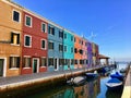 A colourful row of old homes along a canal and beside the sea, on a quiet sunny morning in the beautiful town of Burano, Italy. Royalty Free Stock Photo