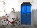 Colourful summer scene of an old red bike outside a greek house with whitewashed walls and a blue painted door in bright sunlight Royalty Free Stock Photo