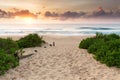 A colourful sunrise over a beautiful ocean scene and a walkway, spotted with footprints in the sand