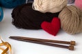 Wooden knitting needles and colored skeins of yarn with a red knitted heart on a white background