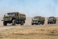 The column consisting of three military trucks Ural carrying soldiers moving across the field