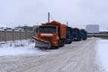 A column of five snow-remover trucks on the road in winter during a snowfall .