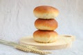 Column of pies with meat laying on wooden board with wheat spikelets in front of them on a grey background, side view