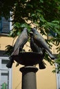 A column, probably a fountain, holds a cup with the sculptures of four pigeons, in Graz.