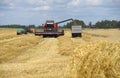 A combine harvester unloads grain into a truck in a field on a summer day.