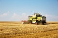 Combine harvester working on a golden ripe wheat field on a bright summer day against blue sky with clouds. Grain dust in the air Royalty Free Stock Photo