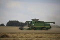 The combine harvests the ripe golden wheat in the grain field. Agricultural work in summer. John Deere green yellow combine