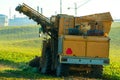 The combine stands on an agricultural field during sunset against the background of the factory. Not environmentally friendly