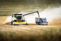 Combine unloading grain into a grain truck while harvesting a barley field during fall harvest with dust trail.