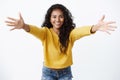 Come here into my arms. Cheerful friendly-looking pretty african american woman in yellow sweater, spread hands in warm Royalty Free Stock Photo