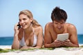 Come join us at the beach. a happy young couple using their tablet and cellphone at the beach.