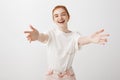 Come to me in warm hugs. Portrait of charming carefree and friendly stylish redhead in pink jeans and t-shirt, pulling