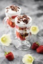 Comfort food. Italian dessert tiramisu with raw strawberries and grated chocolate in Irish glasses on concrete background