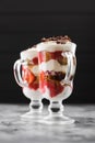 Comfort food. Traditional Italian dessert tiramisu with strawberries in Irish glasses on dark background side view