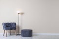 Comfortable armchair, pouf and lamp near wall with space for text. Interior element