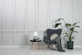 Comfortable armchair, table with lamp and houseplant near light grey wall in room, space for text. Interior design Royalty Free Stock Photo