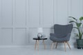 Comfortable armchair, table with lamp and houseplant near light grey wall in room, space for text. Interior design Royalty Free Stock Photo