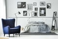 Comfortable blue armchair in monochromatic bedroom interior with king size bed and gallery of posters on the wall Royalty Free Stock Photo
