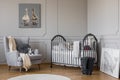 Comfortable grey armchair with round pillow and white blanket next to wooden crib with pillows and toys, copy space on empty wall Royalty Free Stock Photo