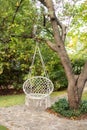 Comfortable hanging wicker white chair in summer garden. Cozy hygge place for weekend relax in garden. Hammock chair in boho style