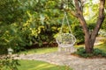 Comfortable hanging wicker white chair in summer garden. Cozy hygge place for weekend relax in garden. Hammock chair in boho style Royalty Free Stock Photo