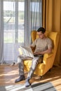 Comfortable home office. A man is sitting and working in a big yellow armchair Royalty Free Stock Photo