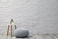 Comfortable knitted pouf, table and decor elements near white brick wall indoors, space for text. Interior design