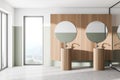 Comfortable two sinks with round mirrors standing on concrete floor in modern bathroom with wooden wall and panoramic windows