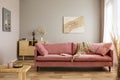 Comfortable velvet pastel pink couch in elegant beige interior with abstract painting