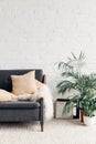 Comfy couch with flowerpots in white living room interior with brick wall