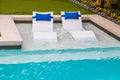 Comfy white loungers in shallow end of refreshing blue swimming pool in yard with flower trim around the edge Royalty Free Stock Photo