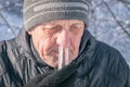Comic concept of a winter cold. Portrait of an elderly man with icicles in his nose. The man`s snot was frozen in his nose. Runny