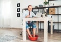 Comic modern office table situation. Businessman typing on laptop keyboard and soaring his feet in Foot hot Bath under table. Dis Royalty Free Stock Photo