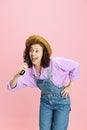 Comic portrait of cheerful young girl, gardener in denim overalls and hat having fun isolated on pink background Royalty Free Stock Photo