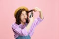Comic portrait of cheerful young girl, gardener in denim overalls and hat having fun isolated on pink background Royalty Free Stock Photo